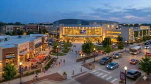 Realistic evening view of the Rock Creek Entertainment District in Norman, Oklahoma, featuring a modern OU performance venue, retail spaces, dining areas, pedestrians, and landscaped streets.